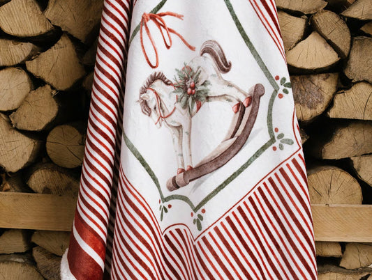Esclusivo plaid natalizio Magic Noel di Nuvole di Stoffa ripiegato nella sua scatola regalo rigida, motivo a righe bianche e rosse con cavallo a dondolo, Tutto Chic.