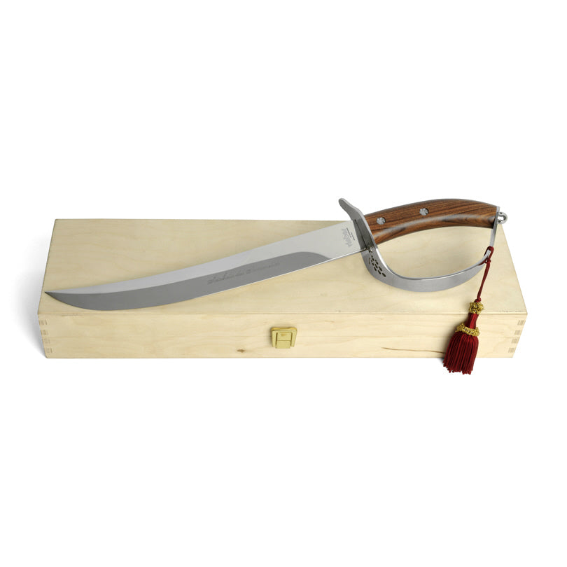 Sciabola per champagne in metallo con manico in legno con cassetta in legno. Il Sabrage è una tecnica per aprire le bottiglie di champagne con una sciabola (sabre in francese), usata solitamente come cerimoniale. Dimensioni cm 51x13/cassetta in legno cm 52x14,5x7,5. In negozio e online su tuttochic.live
