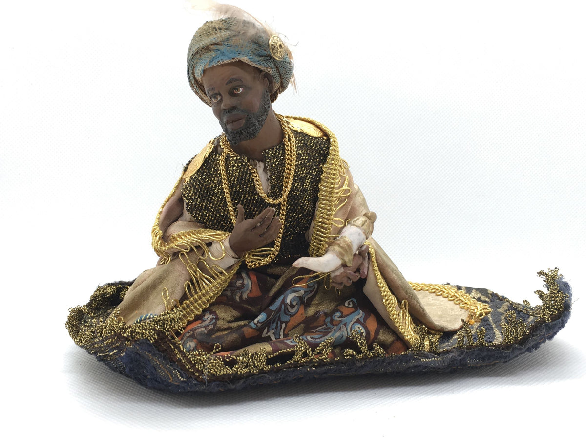Statuina del Re Magio Melchiorre di Angela Tripi seduto su tappeto blu e oro, in terracotta e stoffa con turbante e dono tra le mani, alta 11 cm.
