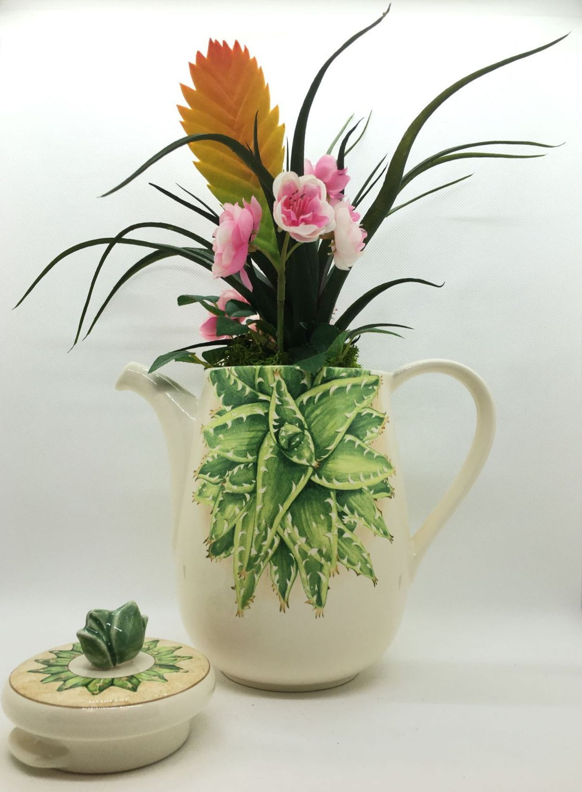 Caffettiera a servire in ceramica decorata con composizione floreale artificiale, completa di coperchio. Made in Italy Dimensioni: (totali cm 30 x 34 h) solo caffettiera cm 20 x 18 h. In negozio e online su tuttochic.live