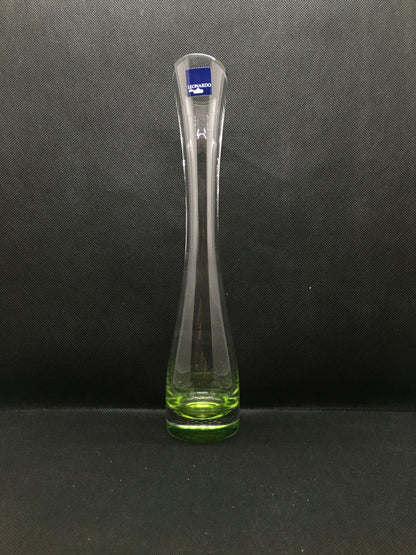 Vasetto monofiore in vetro trasparente con base di colore verde, collo stretto e apertura allargata con taglio obliquo.  Dimensioni: h 27 x 5 cm