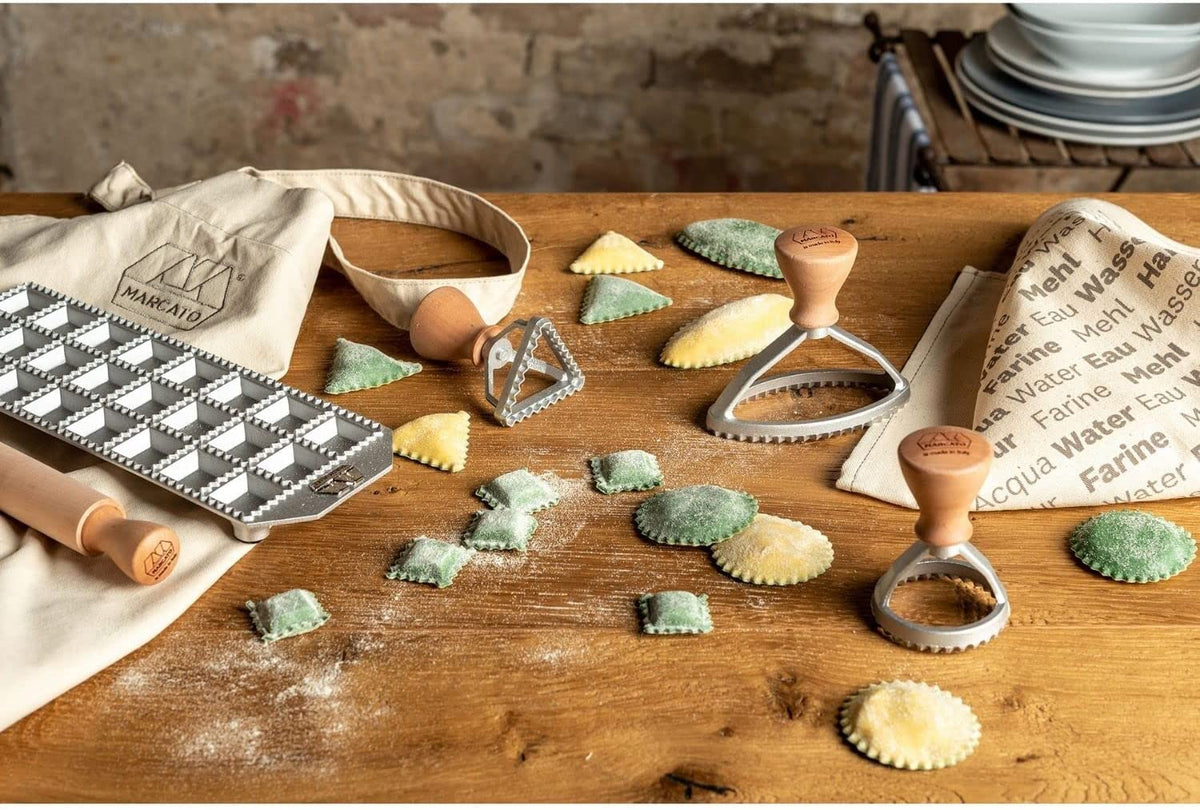 Il set è composto da: tavoletta per 24 ravioli quadrati; mattarello in legno massello di pero; stampino per ravioli tondo 58mm; stampino per raviolo ovale 100 mm stampino per raviolo triangolare 54mm; canovaccio e grembiule  Marcato, 100% cotone; ricettario con piatti internazionali. In negozio e online su tuttochic.live