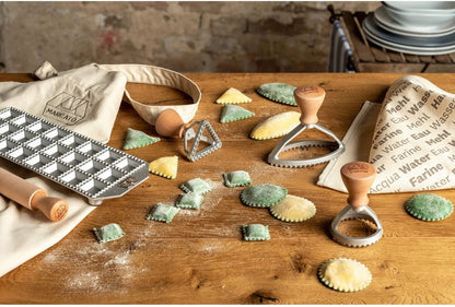 Il set è composto da: tavoletta per 24 ravioli quadrati; mattarello in legno massello di pero; stampino per ravioli tondo 58mm; stampino per raviolo ovale 100 mm stampino per raviolo triangolare 54mm; canovaccio e grembiule  Marcato, 100% cotone; ricettario con piatti internazionali. In negozio e online su tuttochic.live