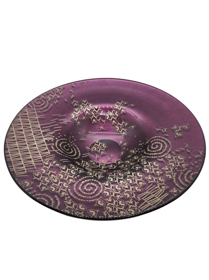 Centrotavola rotondo in vetro di colore ametista con decorazione di colore grigio/argento. Dimensioni: Ø cm 29,5 x 5,5 h. Le piccole imperfezioni che possono essere riscontrate, sono il segno di una lavorazione artistica realizzata completamente a mano. In negozio e online su tuttochic.live