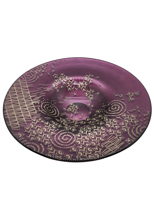 Centrotavola rotondo in vetro di colore ametista con decorazione di colore grigio/argento. Dimensioni: Ø cm 29,5 x 5,5 h. Le piccole imperfezioni che possono essere riscontrate, sono il segno di una lavorazione artistica realizzata completamente a mano. In negozio e online su tuttochic.live