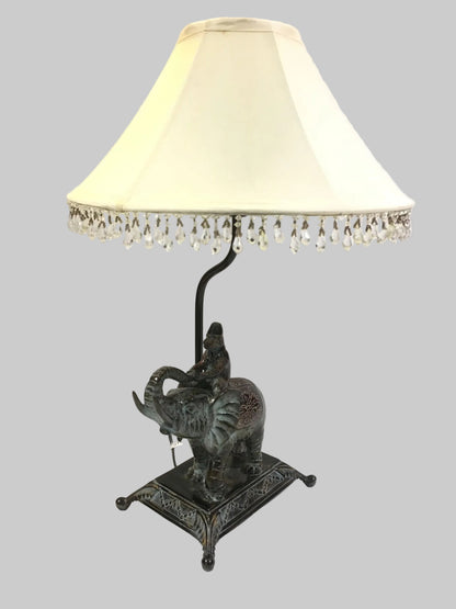 Lampada d'arredo in metallo effetto bronzo di colore verde con paralume in tessuto di colore beige chiaro decorato con strass in acrilico trasparente. Alimentazione: lampadina attacco E27 max 60 W Dimensioni: base cm. 21 x 16 x 55 H - paralume ø 35. In negozio e online su tuttochic.live