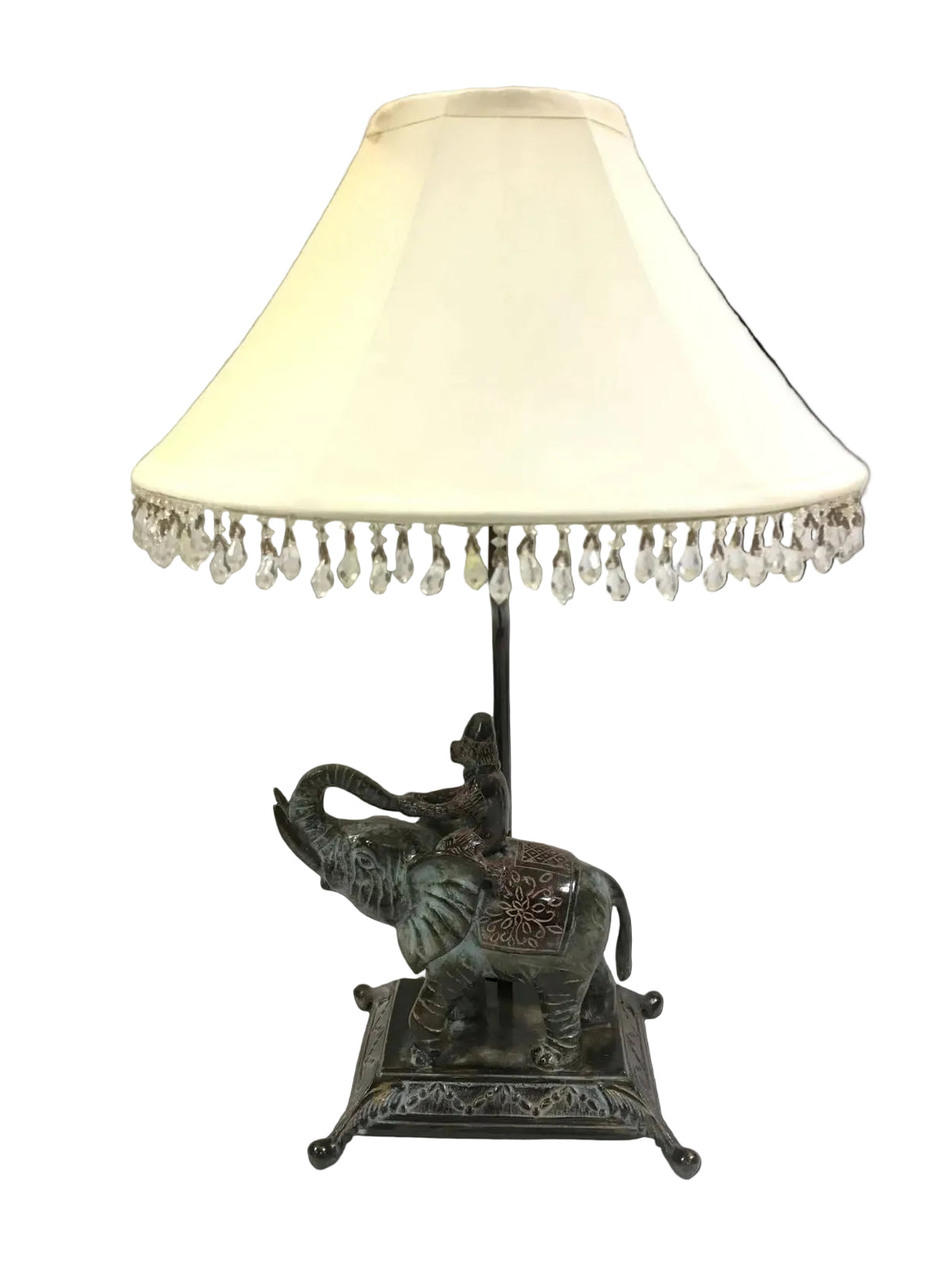 Lampada d'arredo in metallo effetto bronzo di colore verde con paralume in tessuto di colore beige chiaro decorato con strass in acrilico trasparente. Alimentazione: lampadina attacco E27 max 60 W Dimensioni: base cm. 21 x 16 x 55 H - paralume ø 35. In negozio e online su tuttochic.live