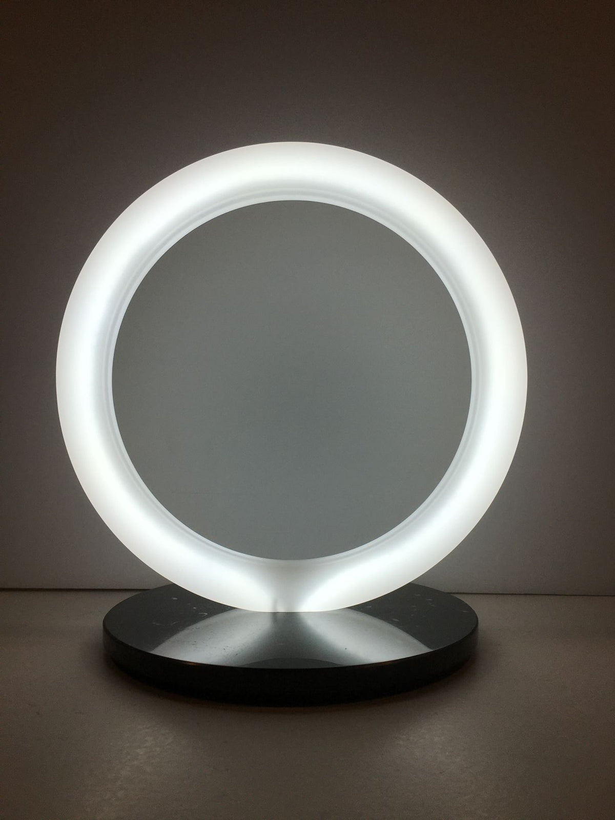 Lampada a forma di anello in cristallo acrilico opalino con base in marmo nero. Dimensioni cm 30 x 23 x 31,5 h. spessore 20 mm anello spessore 15 mm base Tipologia illuminazione led bianco freddo 24v – 8W / Mt Consumo 7W Grado luminosità 7000°K Lunghezza cavo 230 cm con interruttore. In negozio e online su tuttochic.live