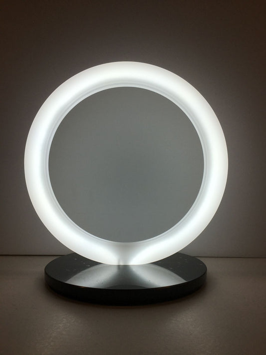 Lampada a forma di anello in cristallo acrilico opalino con base in marmo nero. Dimensioni cm 30 x 23 x 31,5 h. spessore 20 mm anello spessore 15 mm base Tipologia illuminazione led bianco freddo 24v – 8W / Mt Consumo 7W Grado luminosità 7000°K Lunghezza cavo 230 cm con interruttore. In negozio e online su tuttochic.live