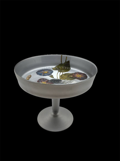 Alzata in vetro di colore argento con decorazione floreale. Dimensioni: Ø cm 18,5 x 15,5 h Decorata a mano in Italia, lavare a mano. In negozio e online su tuttochic.live